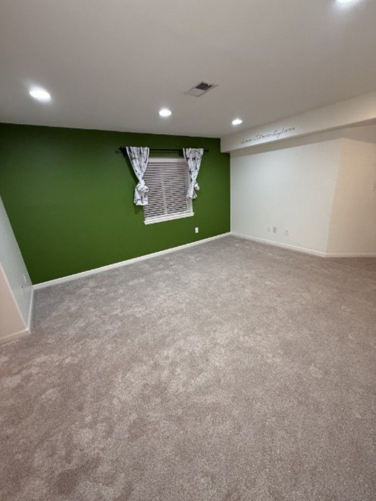 Empty carpeted room with green accent wall and small window covered by curtain.