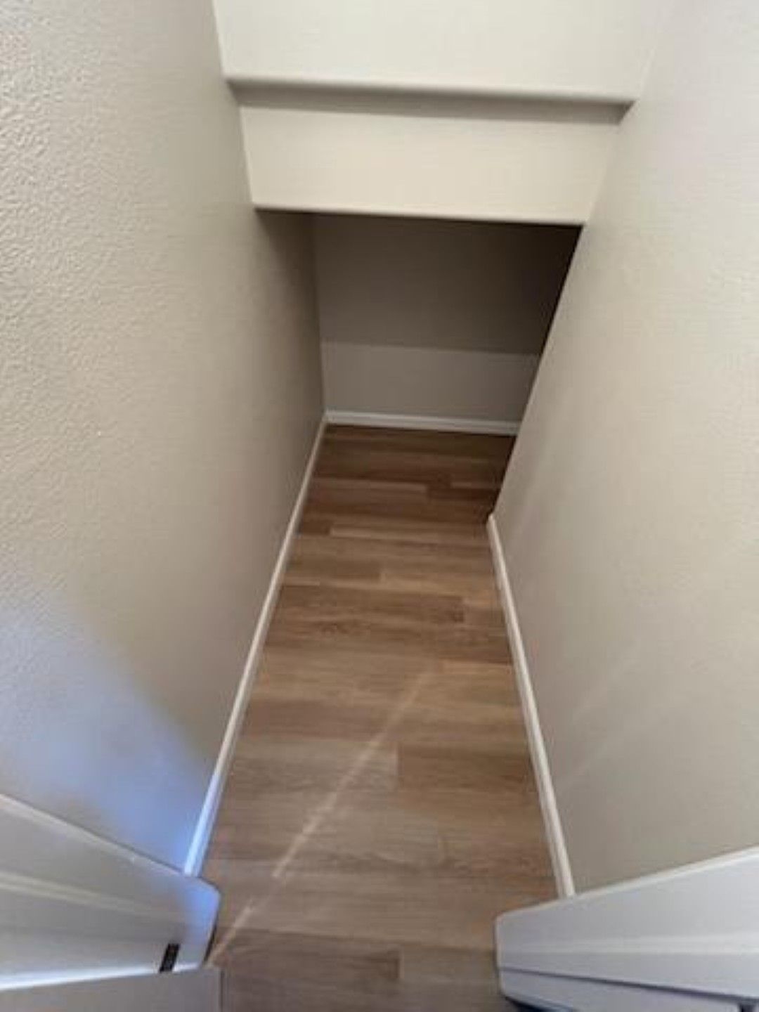 Narrow carpeted stairwell under a low overhang, with white walls and wood-pattern flooring.