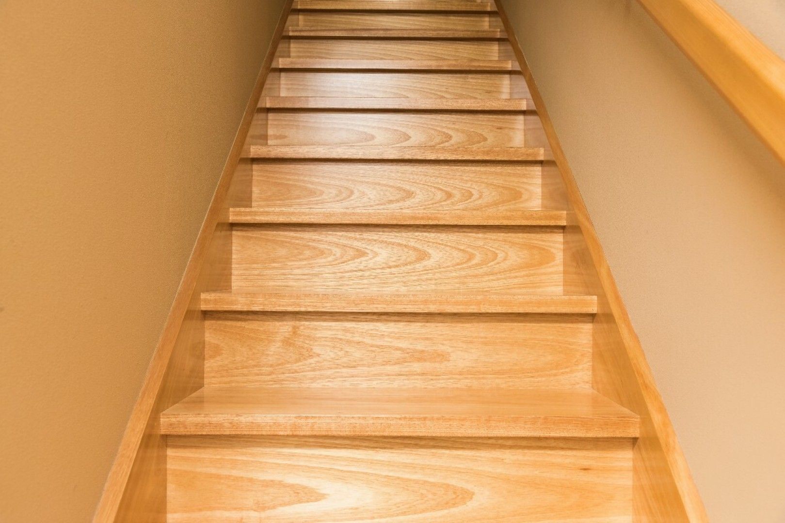 Wooden staircase viewed from below, leading upward between beige walls.