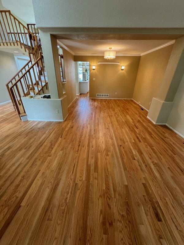 Empty living room with hardwood floors, staircase, and chandelier in a beige interior