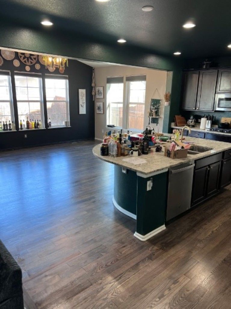 Modern kitchen and open living area with dark cabinets, island countertop, and wood flooring.