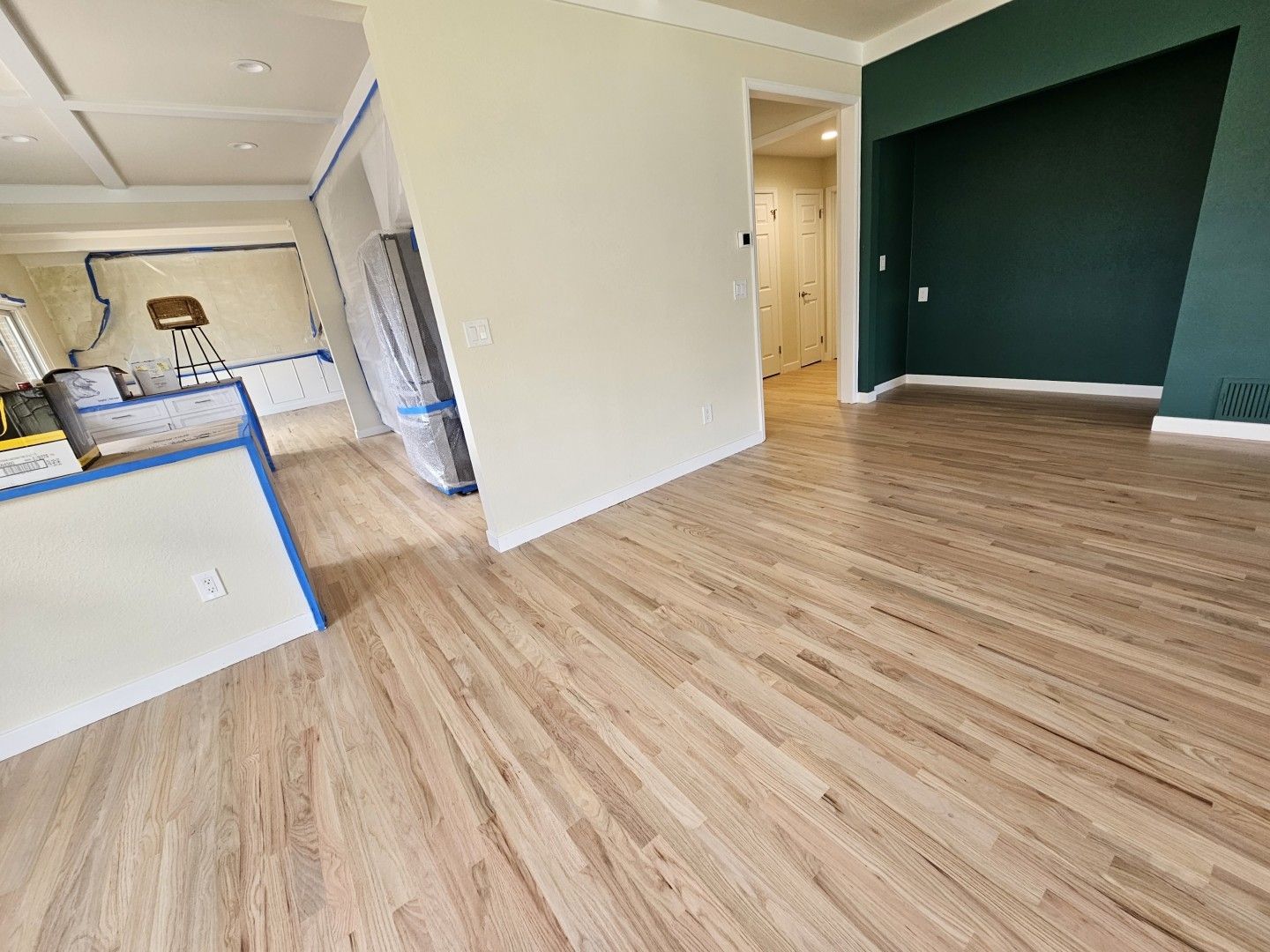 Empty modern bedroom with wood floors, dark green accent wall, and a doorway to a hall