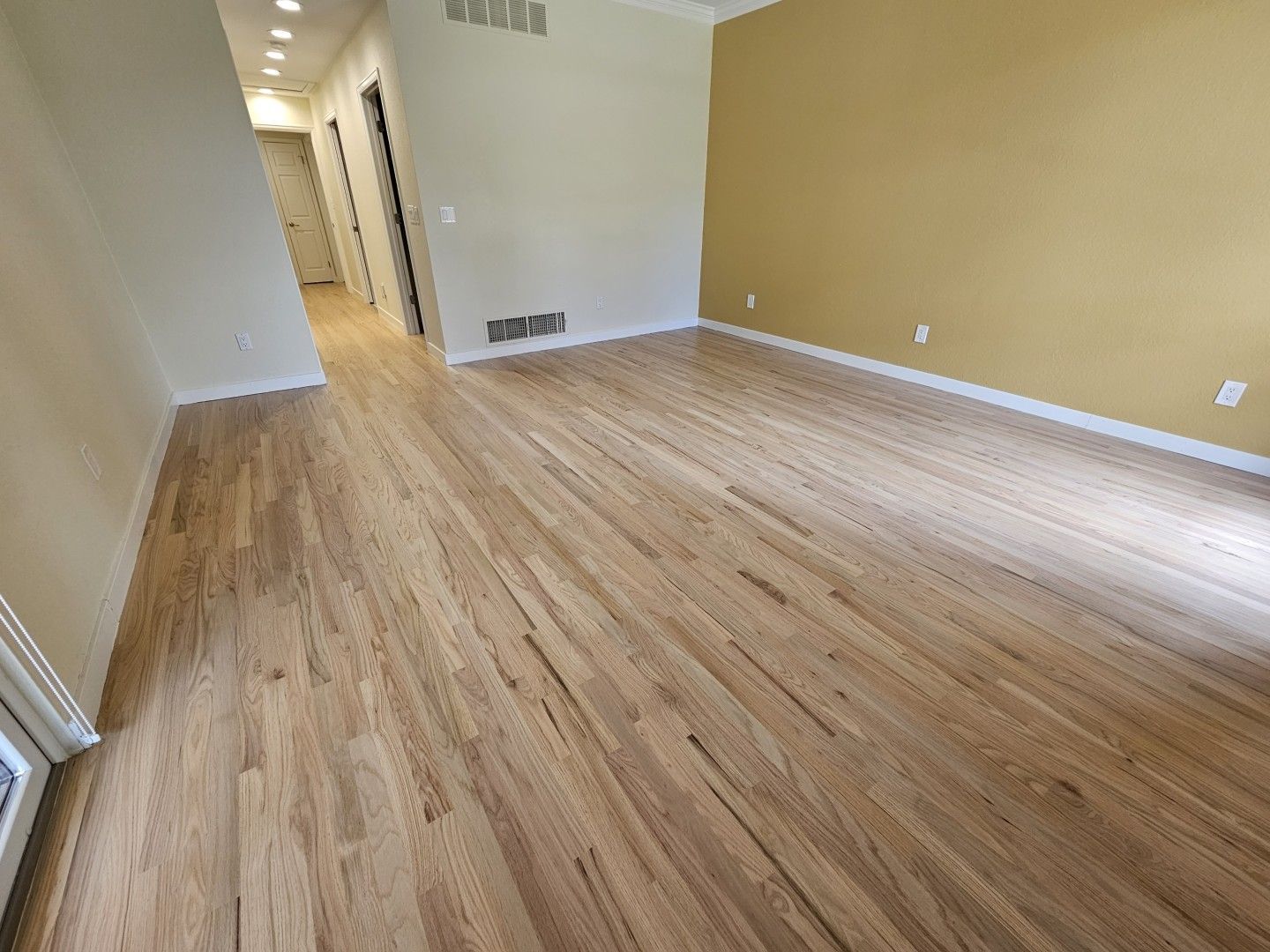 Empty beige room with wood-look flooring and a hallway in the background