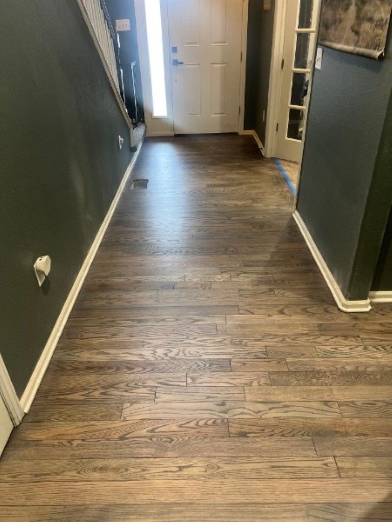 Narrow hallway with dark walls, wood flooring, and a white front door at the end.