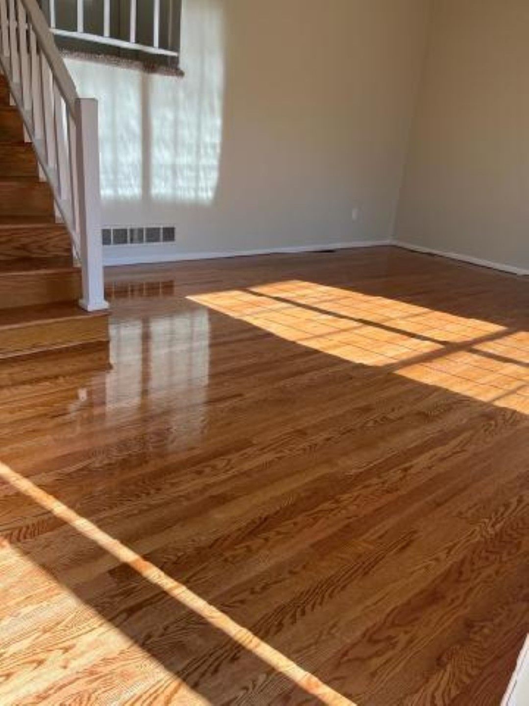 Empty room with polished hardwood floor, staircase, and sunlight streaming through a window
