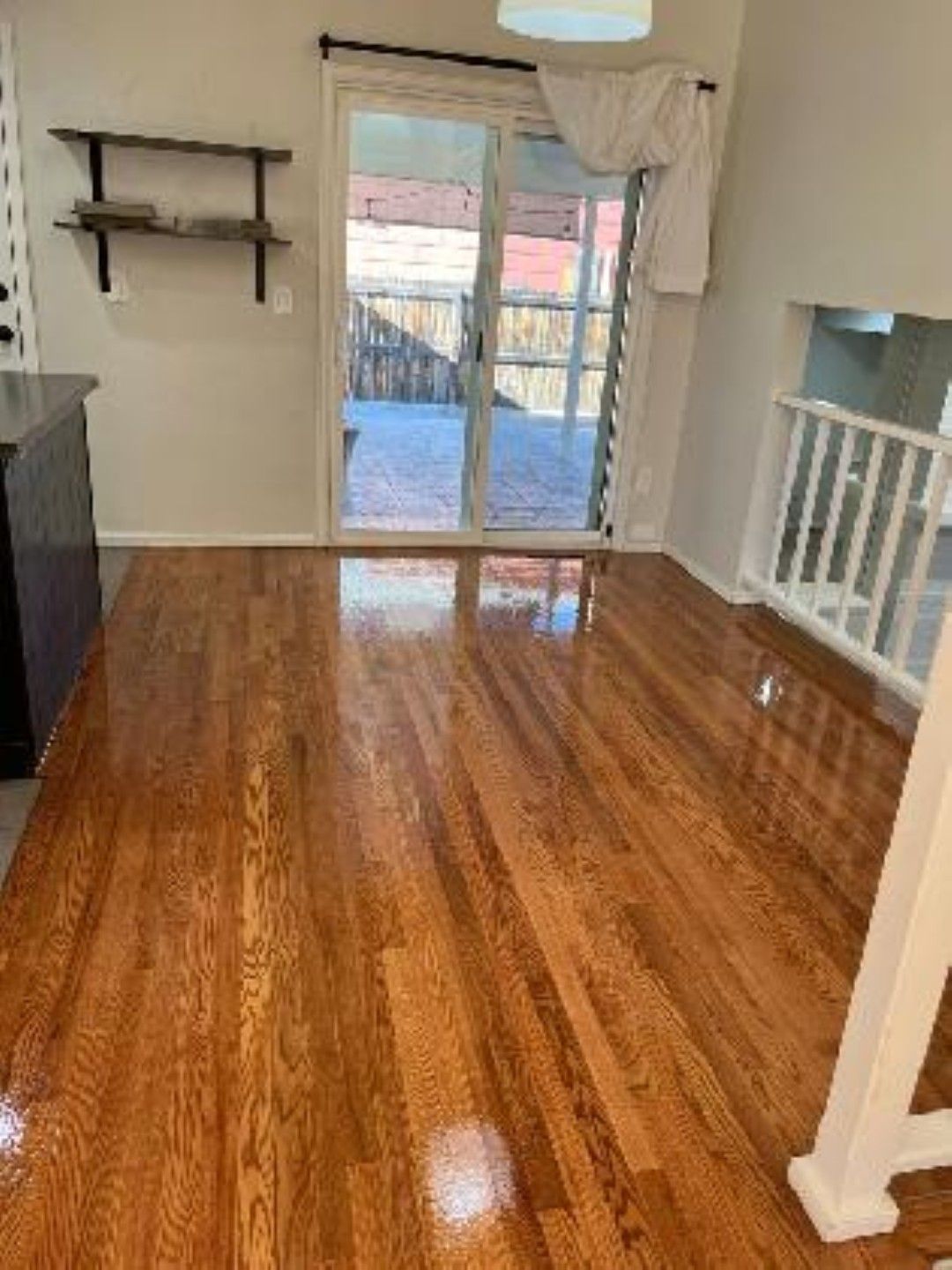 Empty living room with glossy hardwood floors, sliding glass doors, wall shelves, and a fireplace opening.