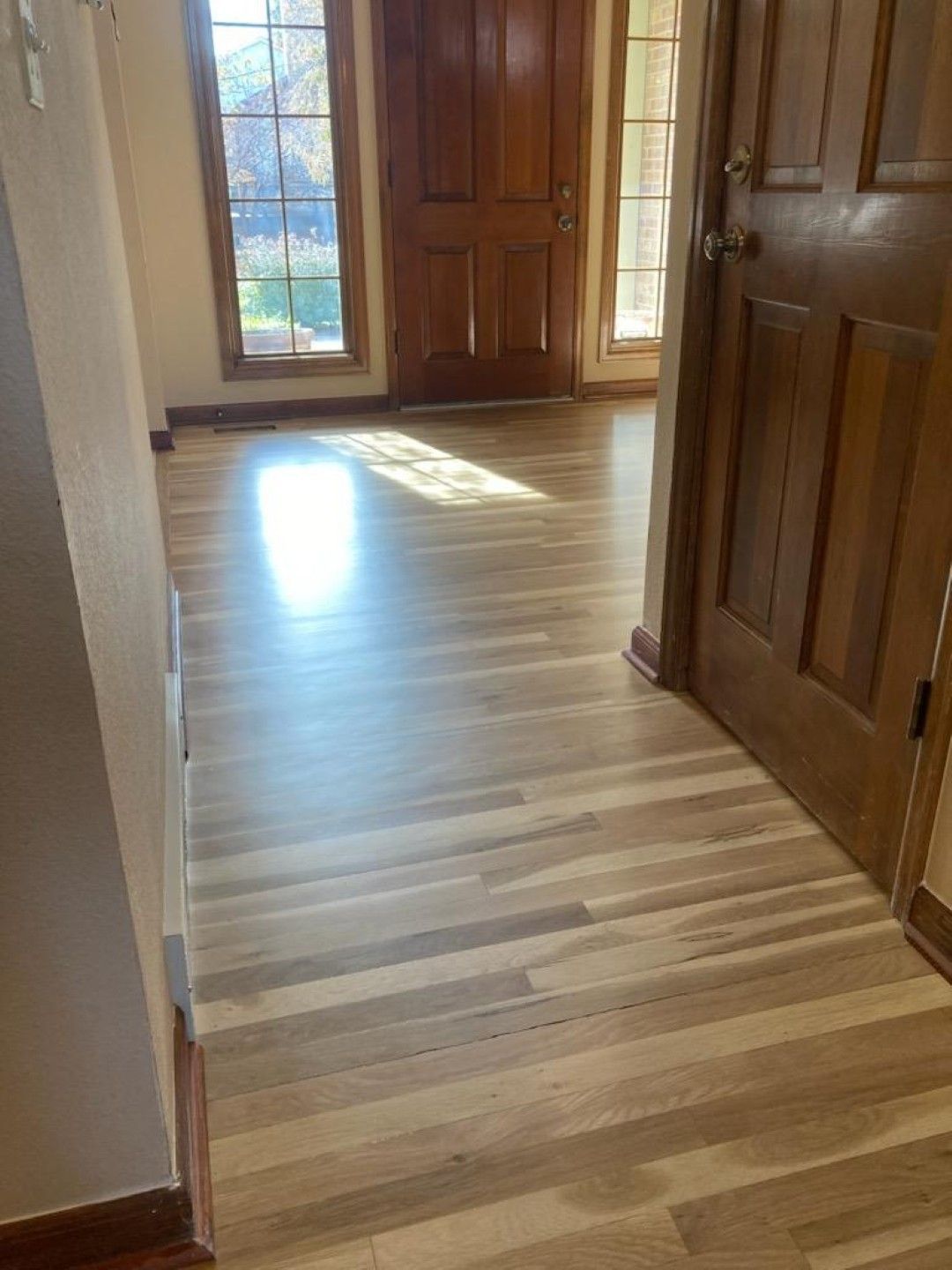 Sunlit hardwood hallway with wooden doors and a glass door at the end