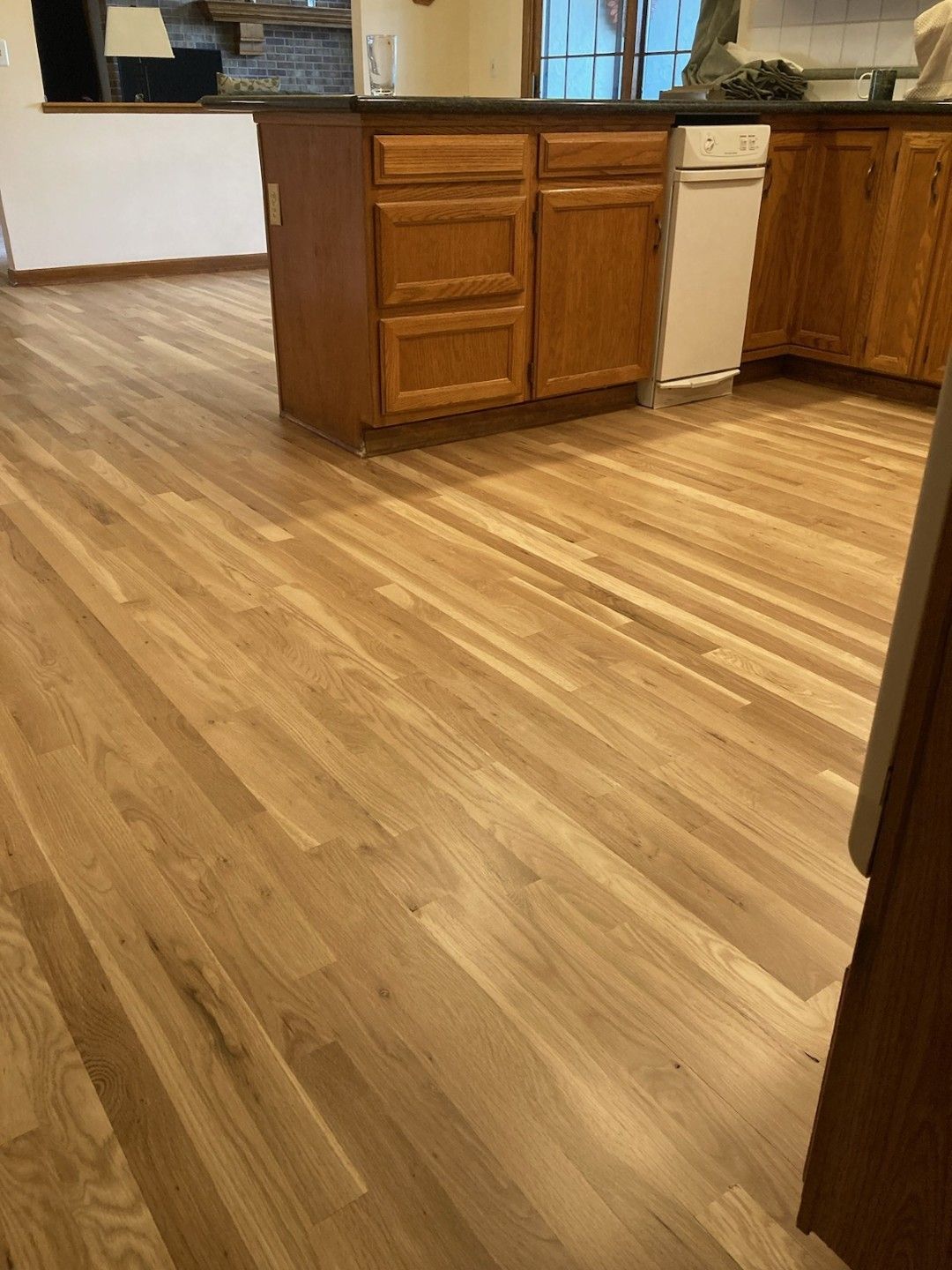 Empty kitchen with wood cabinets and hardwood floor; white dishwasher visible.