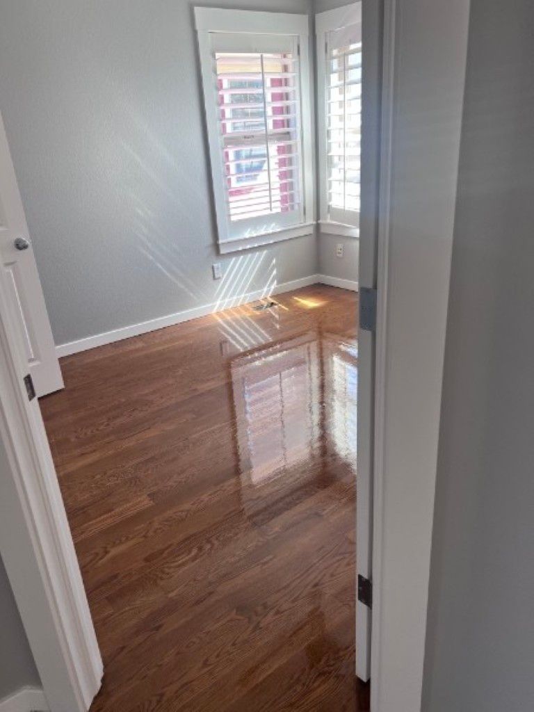 Empty room with gray walls, glossy hardwood floors, and sunlight streaming through window shutters.