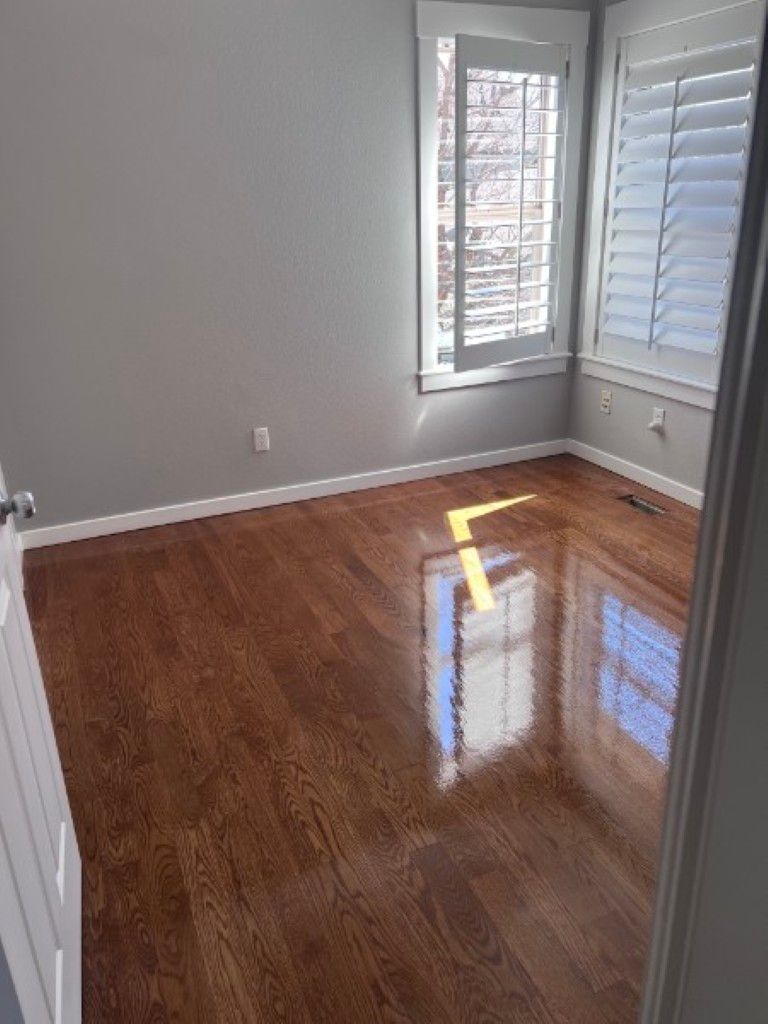 Empty room with hardwood floors, gray walls, and two windows with white shutters.