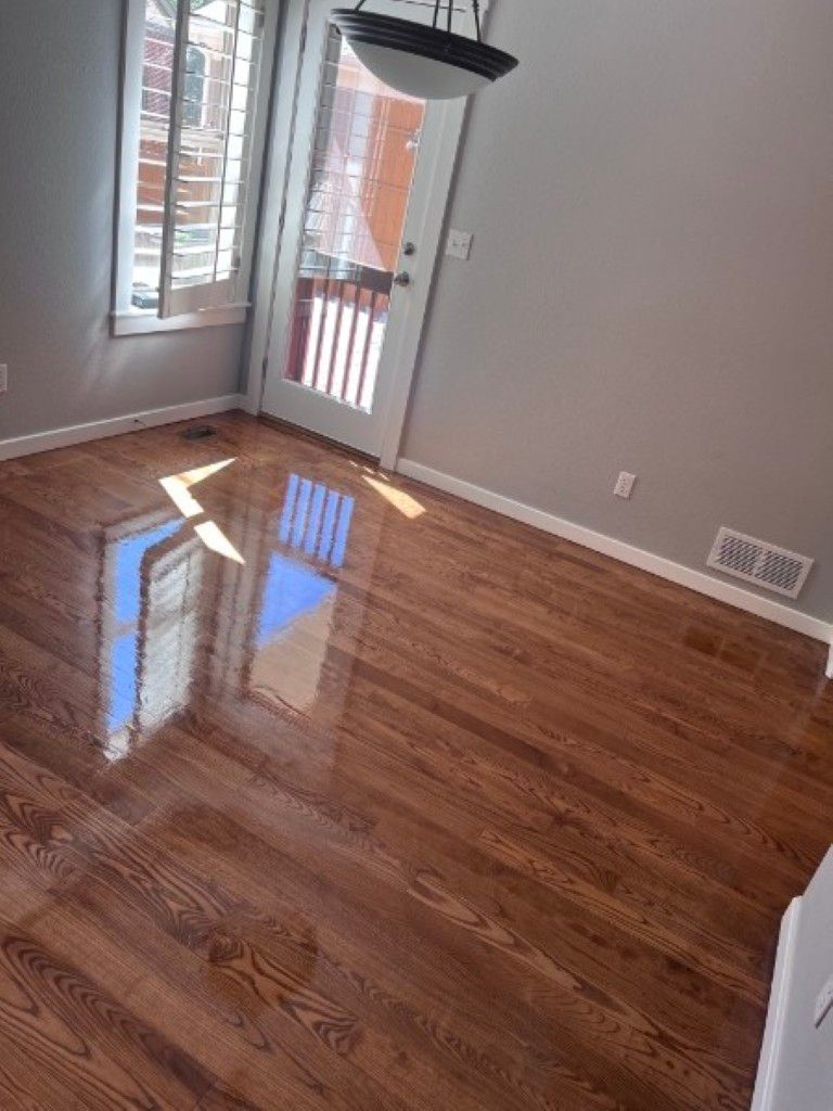 Empty room with glossy hardwood floors, gray walls, window, and open door letting in sunlight.