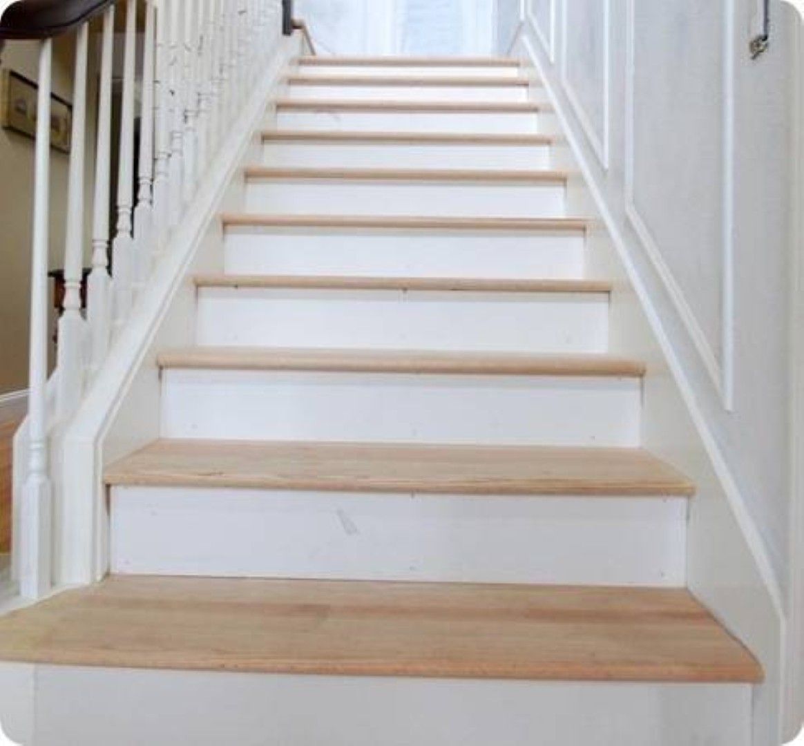 White staircase with light wood treads and white railings in a bright hallway