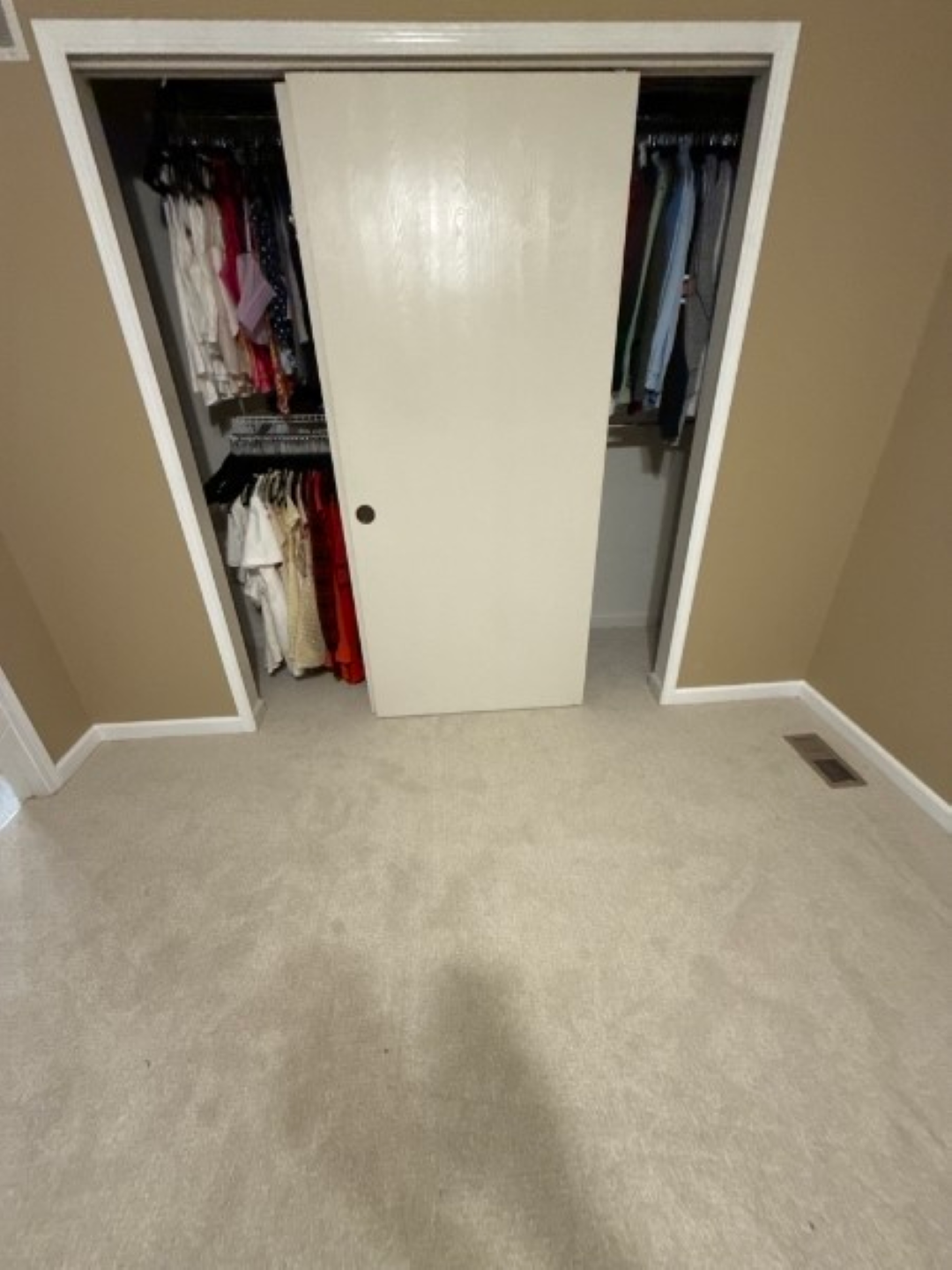 Open closet with white sliding door, clothes on both sides, in a beige-carpeted bedroom