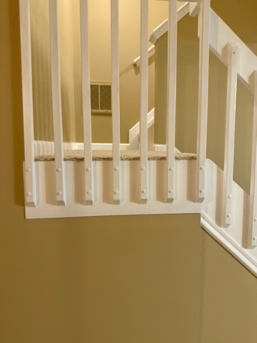 Indoor stair landing with white balusters and beige walls, viewed from above