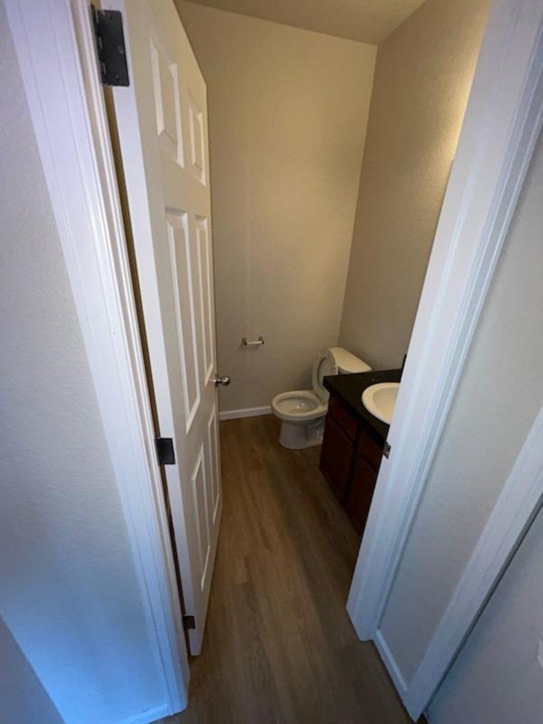 Narrow bathroom hallway with toilet and sink vanity; white walls and wood-look floor.