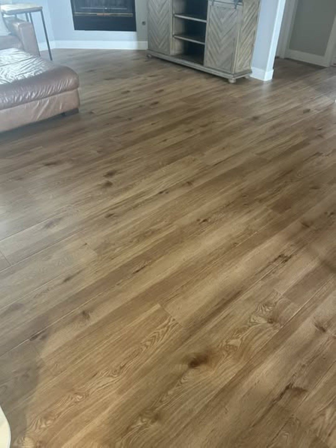 Empty living room with wood flooring and a tan leather couch against the wall