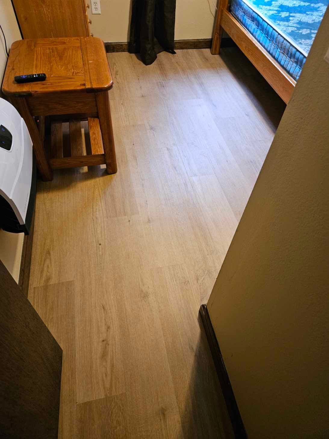 Narrow room with light wood floor, small wooden stool, and bed beside a blue curtain.