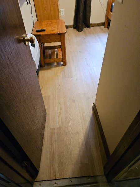 Narrow hallway with wood flooring, an open door, and a small wooden bench near a curtain.