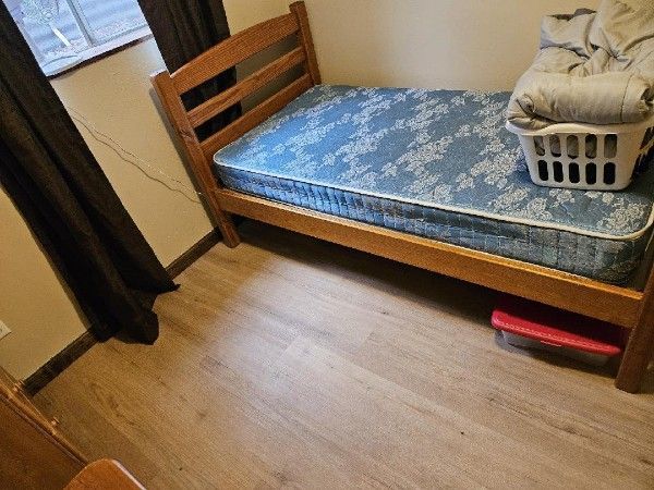 Small bedroom with a wooden bed, blue patterned mattress, and laundry basket on top.