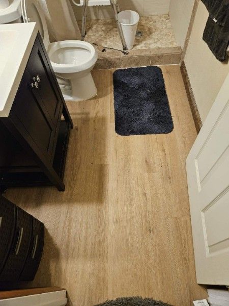 Small bathroom with toilet, vanity, dark bath mat, and light wood-look floor.