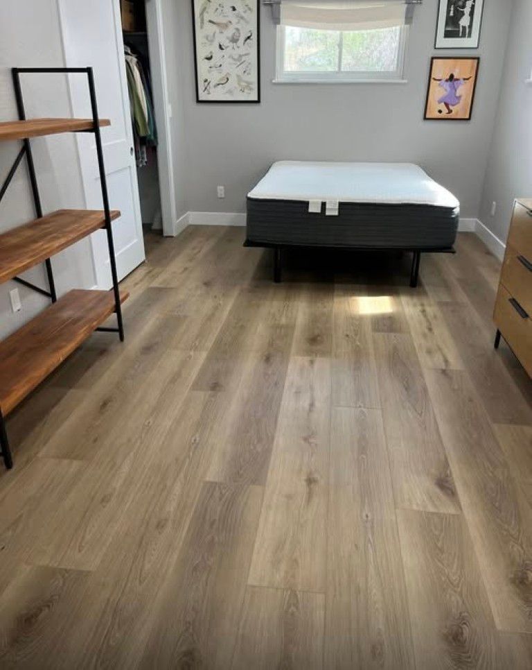 Empty bedroom with wood flooring, gray walls, a bed, window, wall art, and a small dresser.
