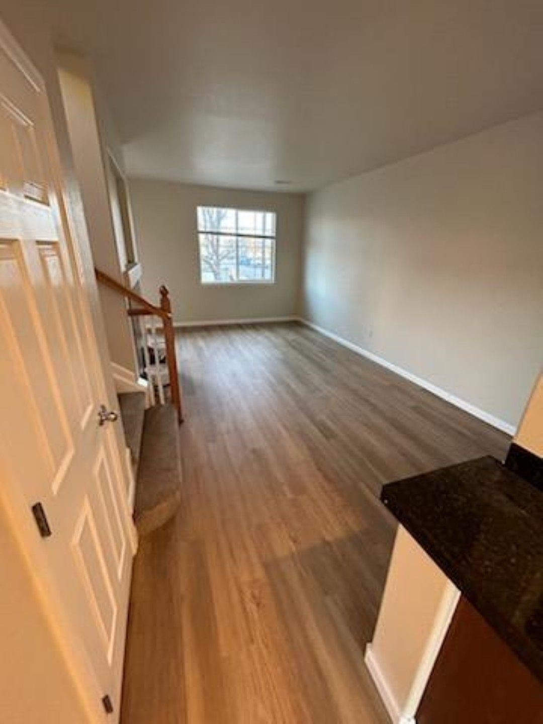 Empty living room with wood floors, white walls, and a window at the far end.