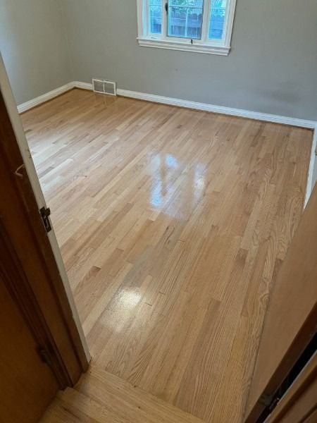 Empty room with light wood floors, beige walls, and a window letting in daylight