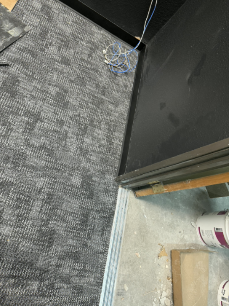 Carpeted floor beside a black cabinet, with loose blue cable near the corner.