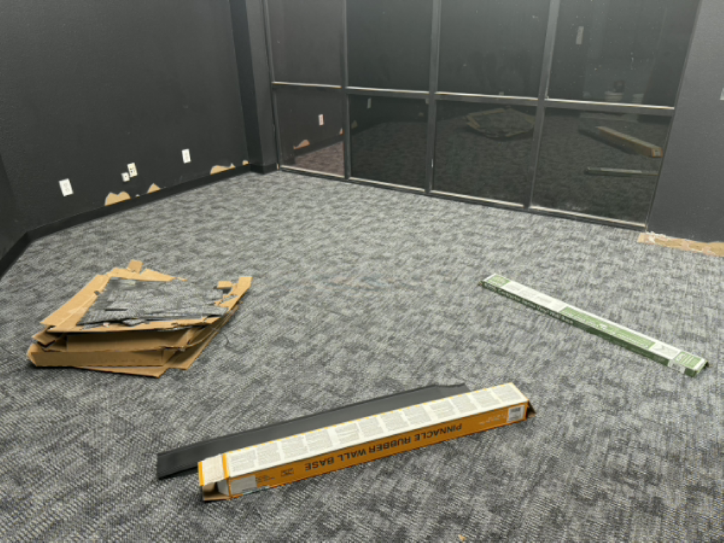 Empty office room with carpet, black walls, and scattered wooden boards and trim on the floor.
