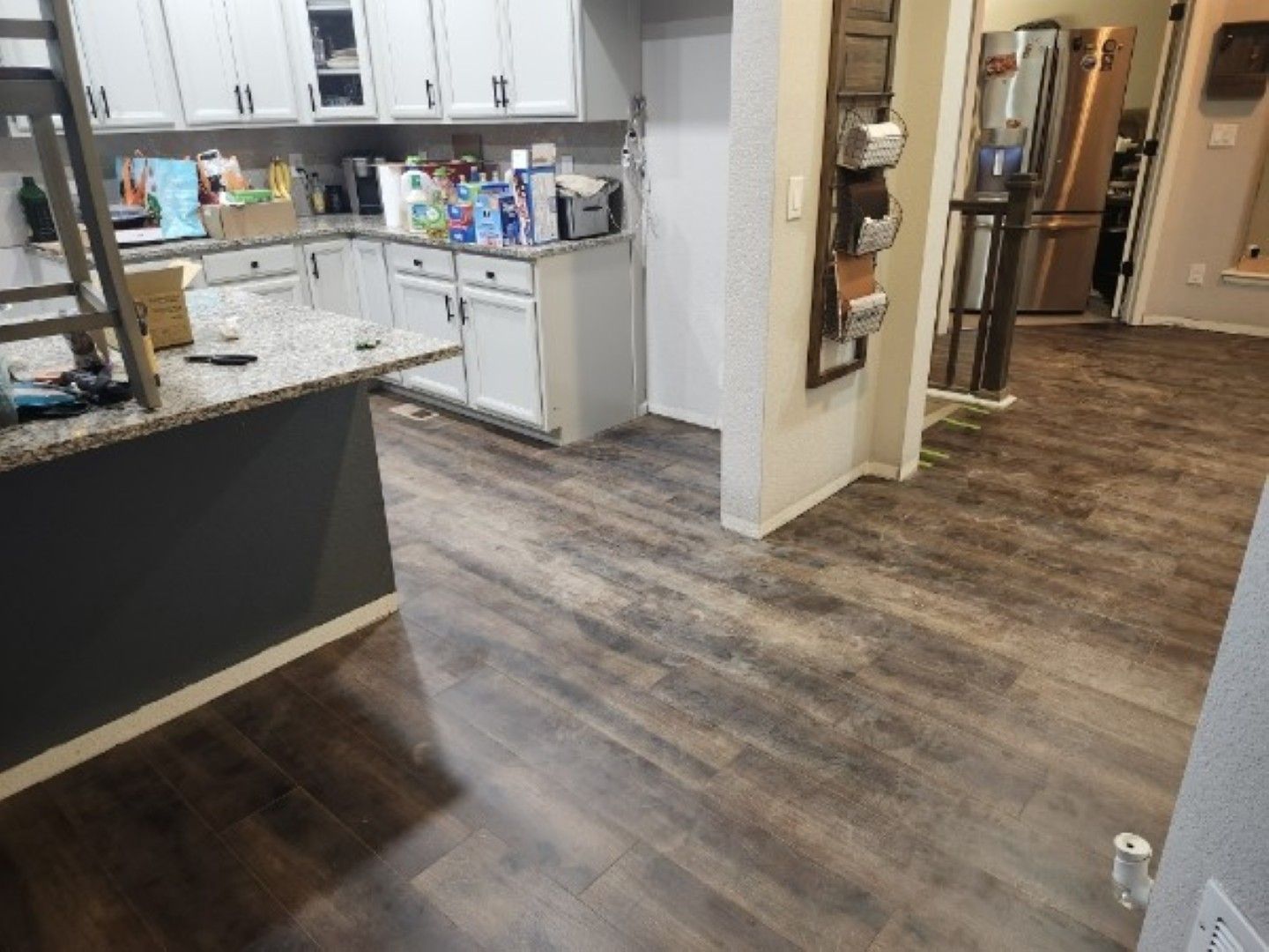Open kitchen and hallway with wood-look flooring, white cabinets, and a granite countertop.