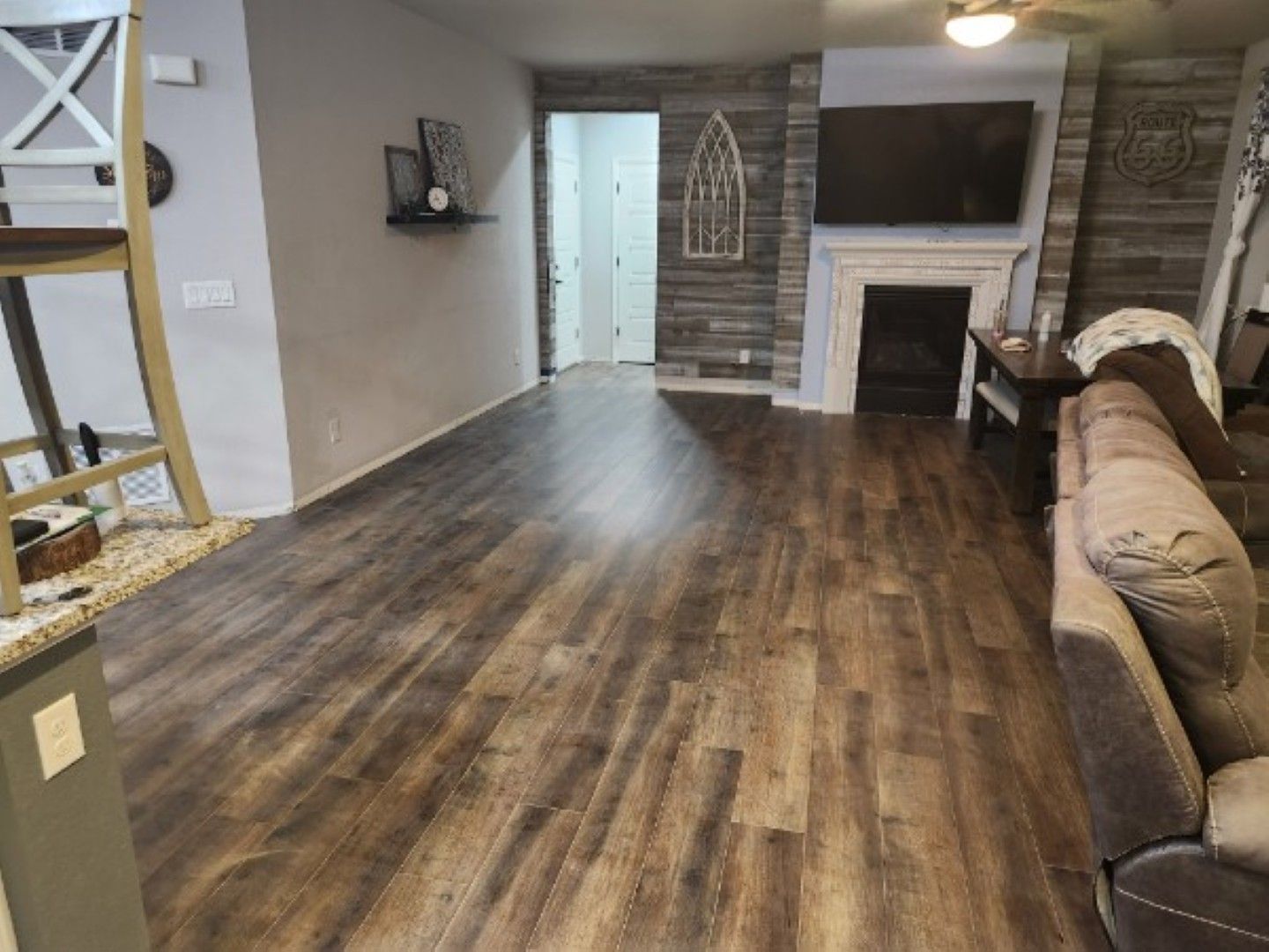 Empty living room with wood-look floors, white fireplace, tan sofa, and open doorway.