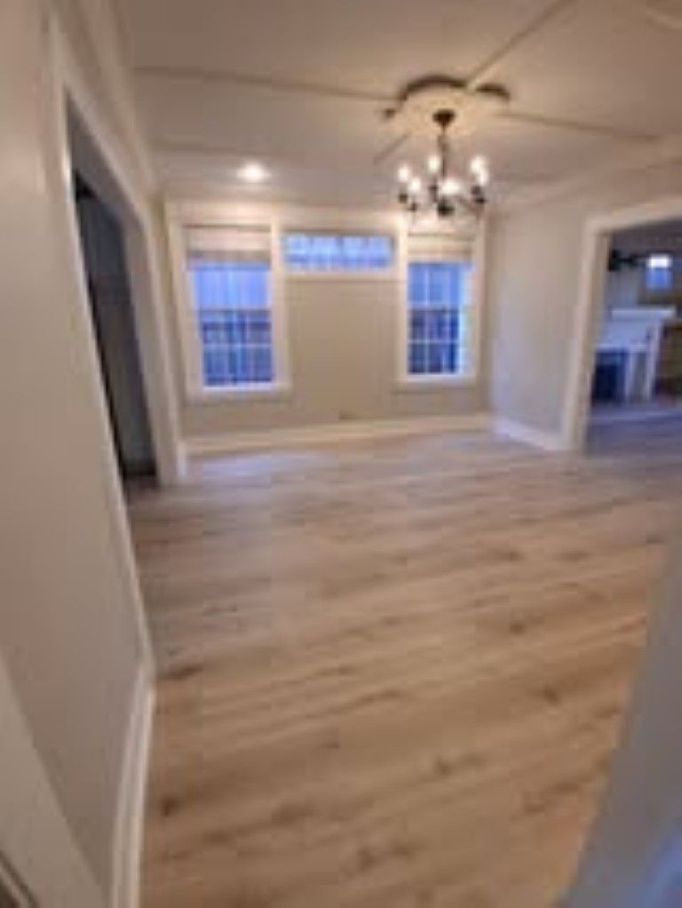 Empty dining room with light wood floors, white walls, and large windows under a chandelier.