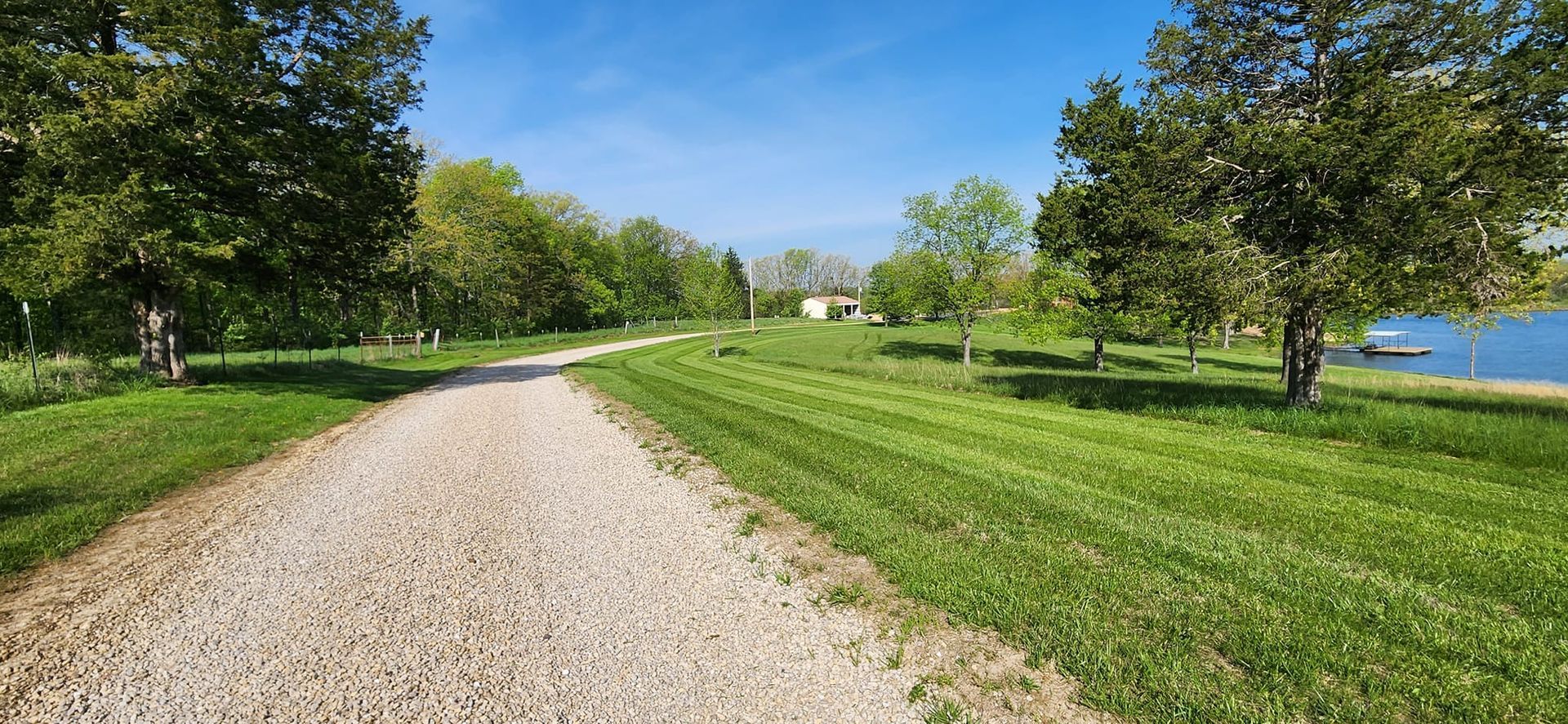 A gravel road leading to a lake surrounded by trees and grass.