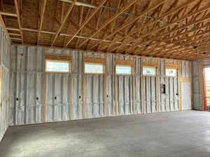 Interior of a building under construction showing foam-insulated walls, multiple high windows, and open wood ceiling joists.