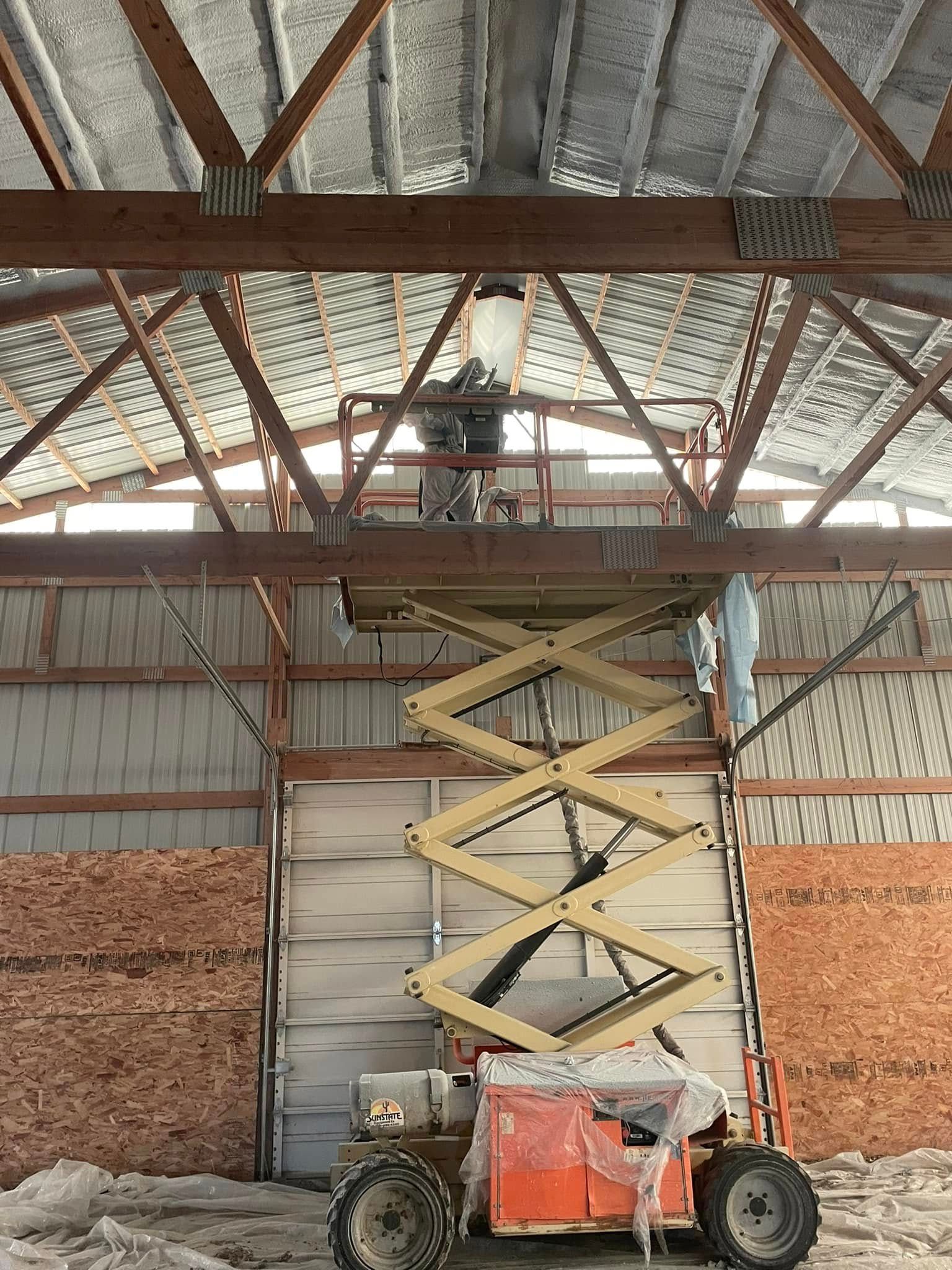 A person in a scissor lift works near the metal-paneled ceiling of an unfinished, industrial-style building.