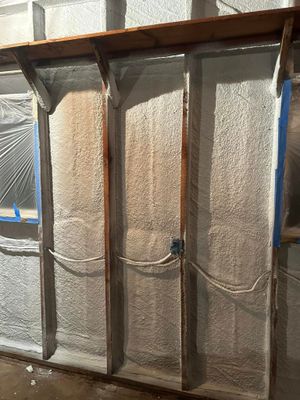 Interior wall studs and a top plate covered in rough, light-colored spray foam insulation with electrical wiring.