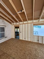An interior view of a room under construction with exposed wooden framing, spray foam insulation, and OSB flooring.