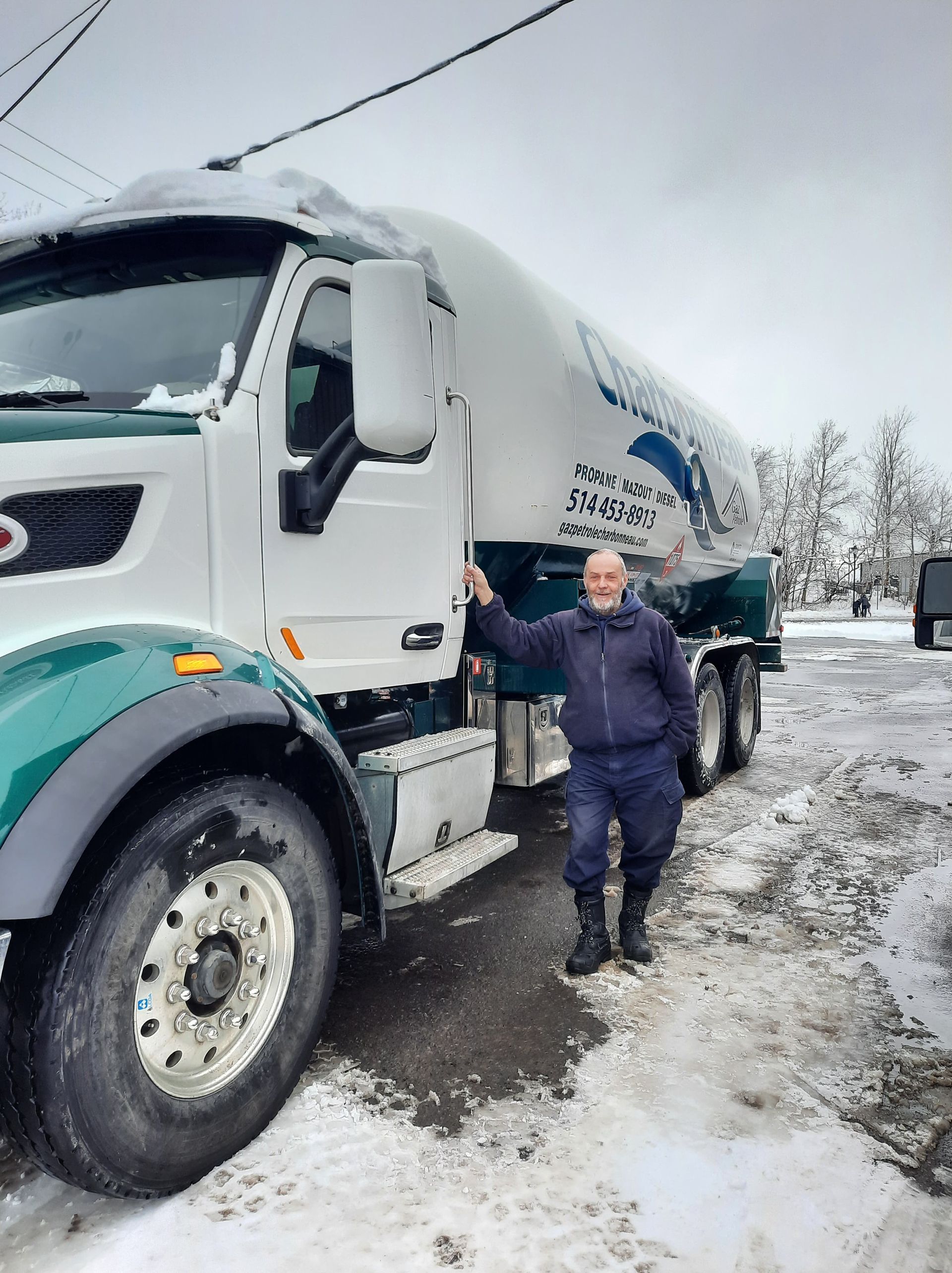Un homme se tient à côté d'un camion-citerne blanc et turquoise par une journée enneigée.