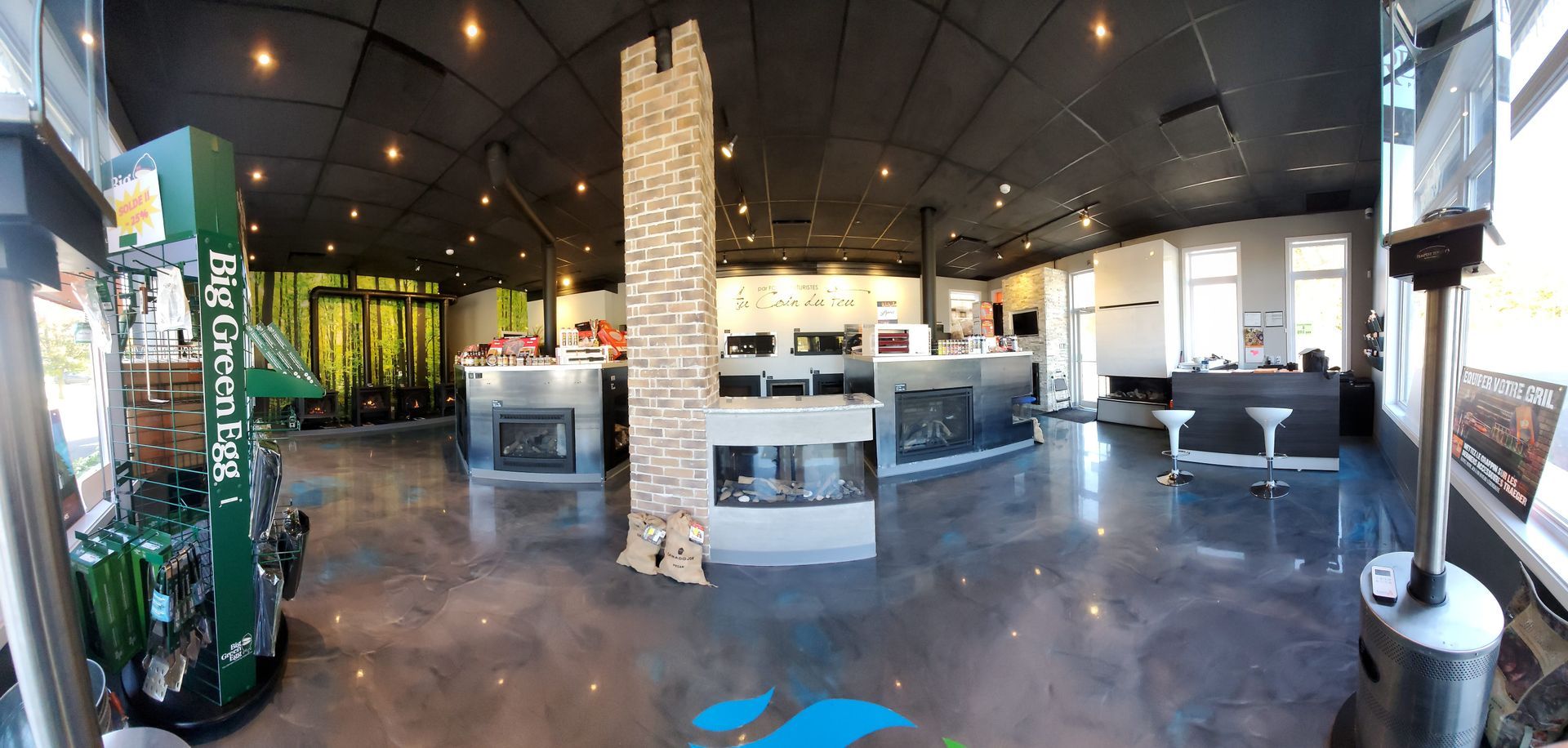 Interior of a showroom with fireplaces and a central stone pillar. Green display and bar in view.