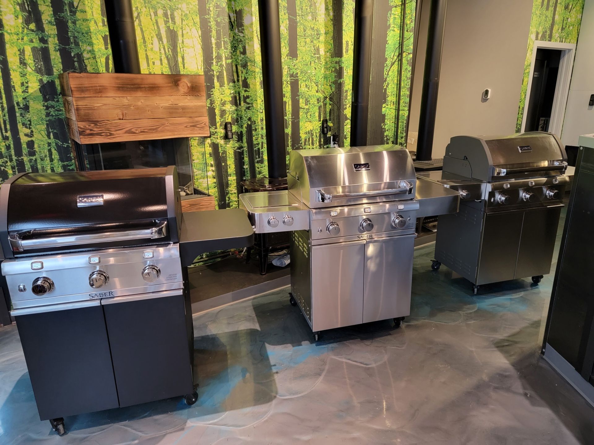 Three stainless steel gas grills of different sizes in a showroom setting.