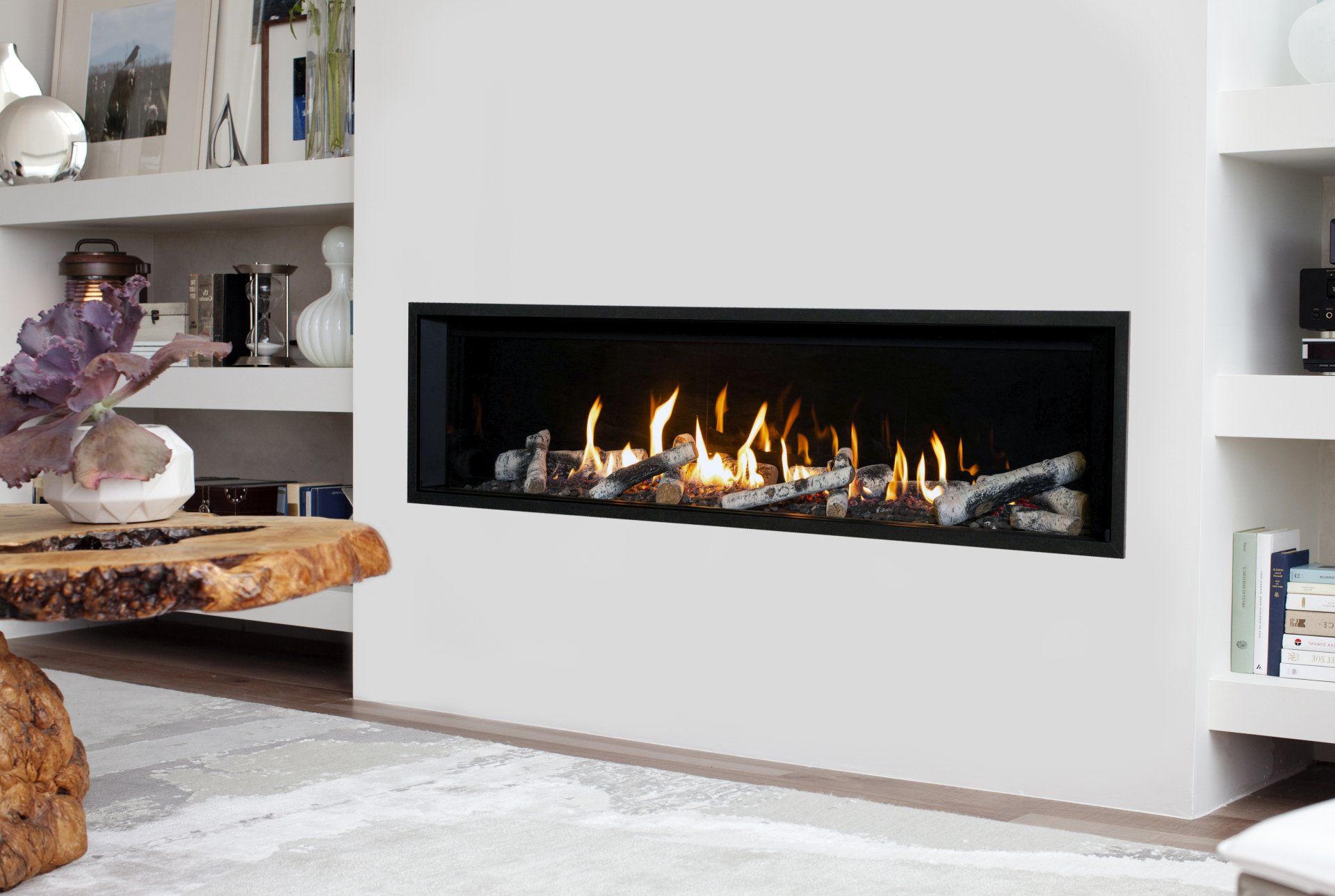 Cheminée moderne encastrée dans un mur blanc, bûches et flammes à l'intérieur, avec étagères.