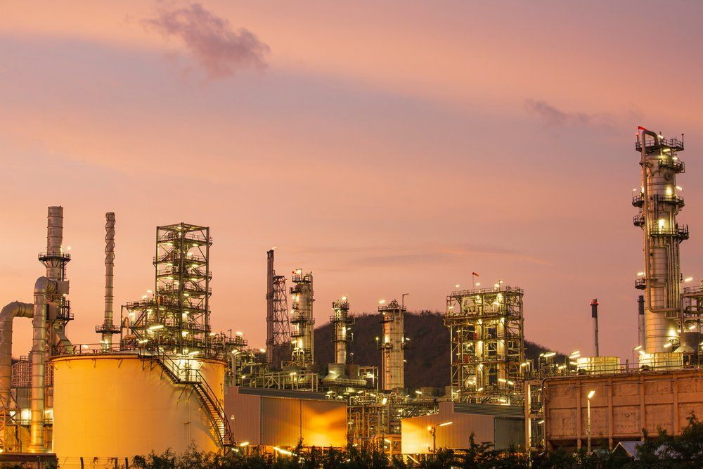 Raffinerie de pétrole au coucher du soleil, avec des lumières vives sur un ciel rose et orange.