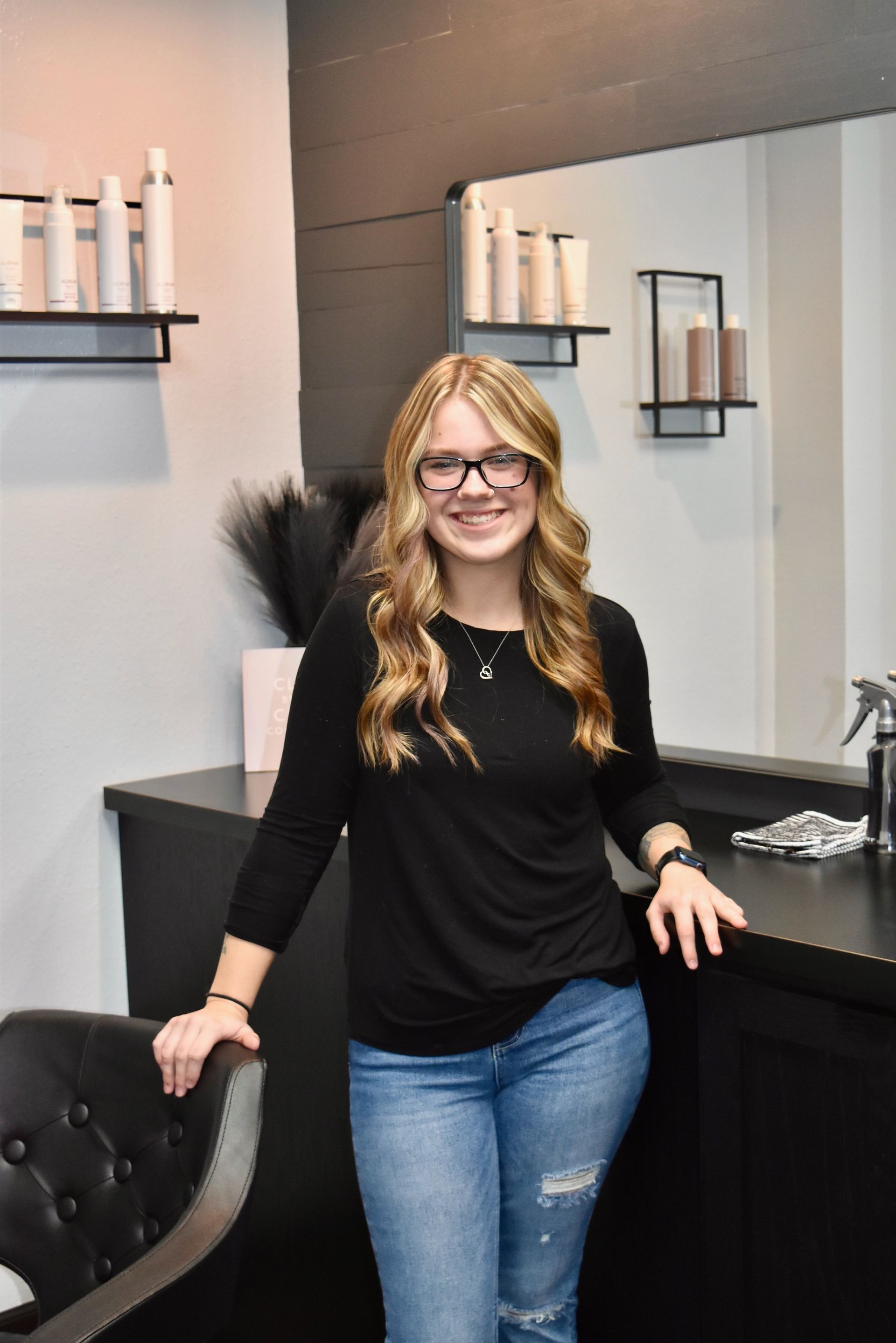 A woman wearing glasses and a black shirt is standing in a salon.