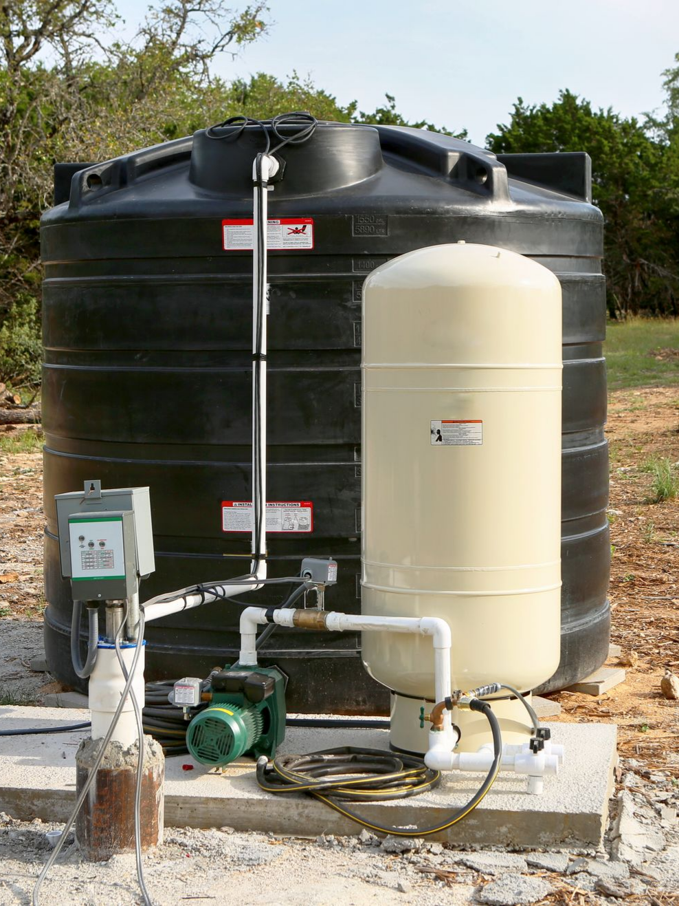 Water pump and filtration tanks beside a large black water storage tank outdoors