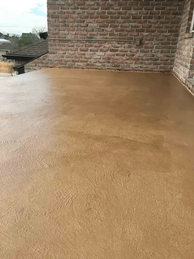 A freshly poured, smooth tan-colored concrete surface adjacent to a rustic red brick wall.