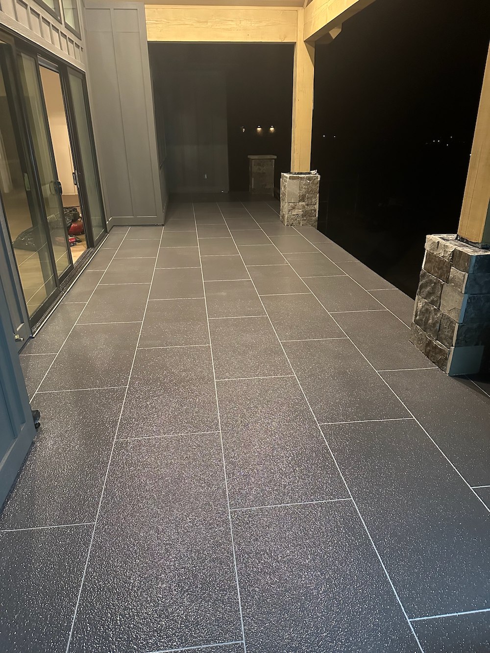 A paved outdoor walkway made of dark, speckled stone tiles leading toward an open dark entrance.