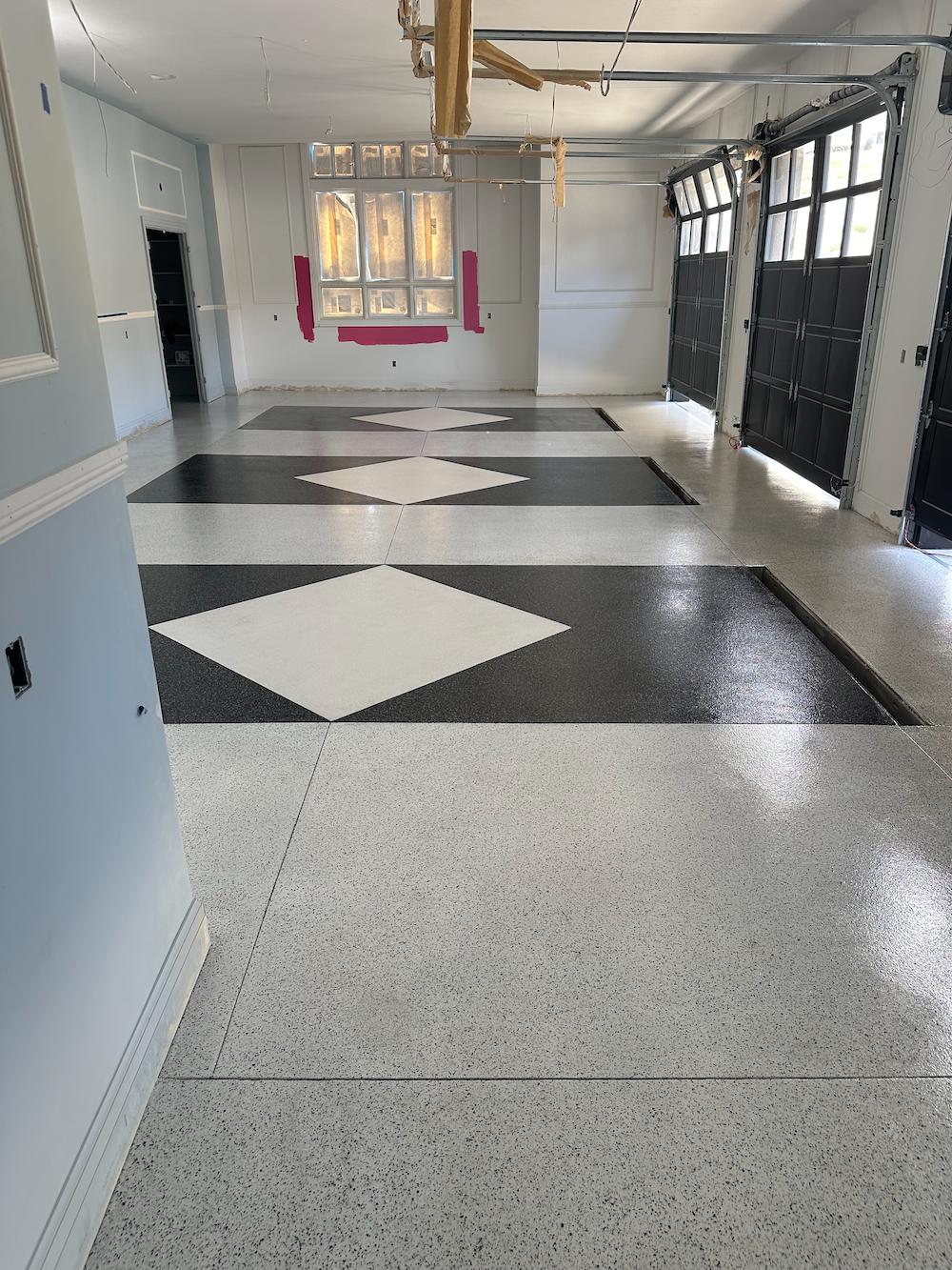 A garage floor with a speckled gray base, featuring three large black rectangles with white diamond centers.