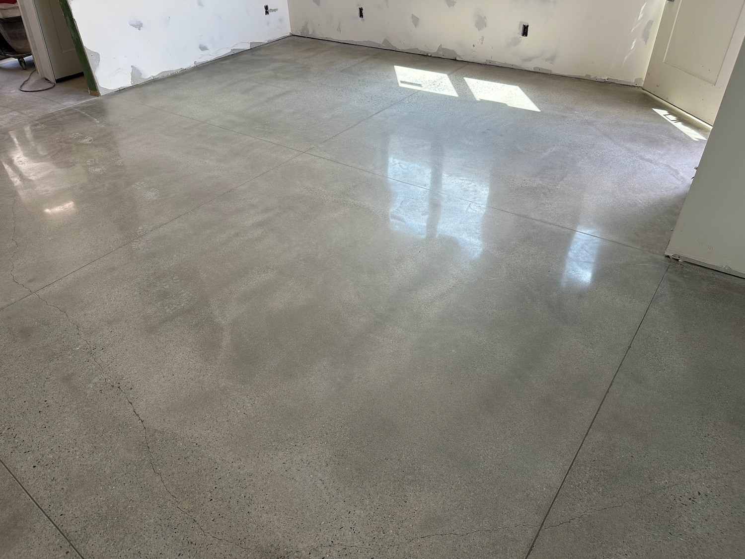 A polished, light gray concrete floor in an unfinished room with white walls.