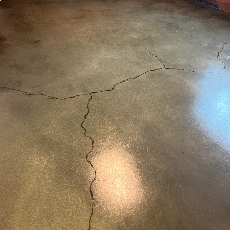 A large, Y-shaped crack spreads across a grey, polished concrete floor.
