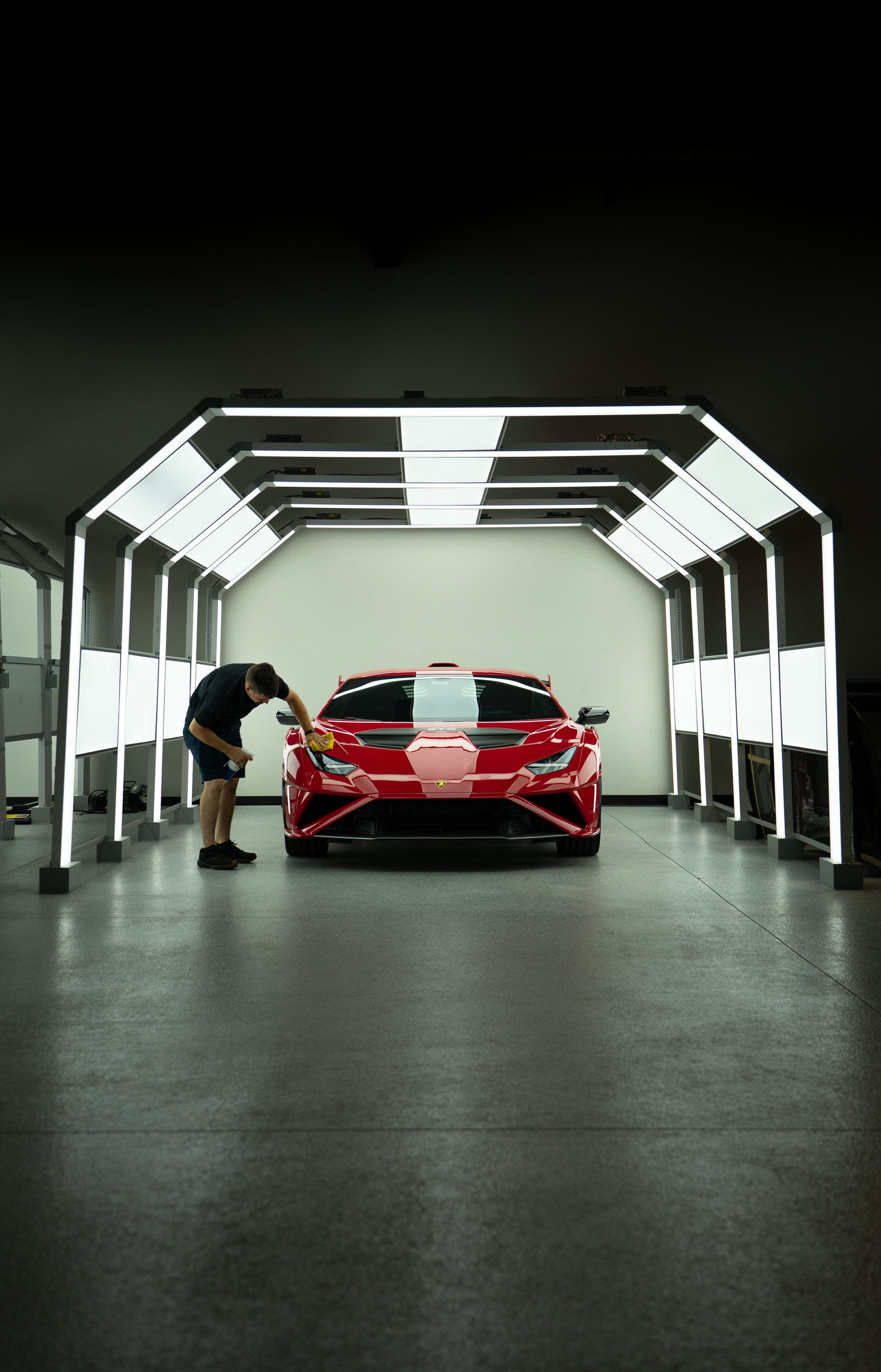 Red sports car in a lit garage tunnel, with a person leaning near the front left side.